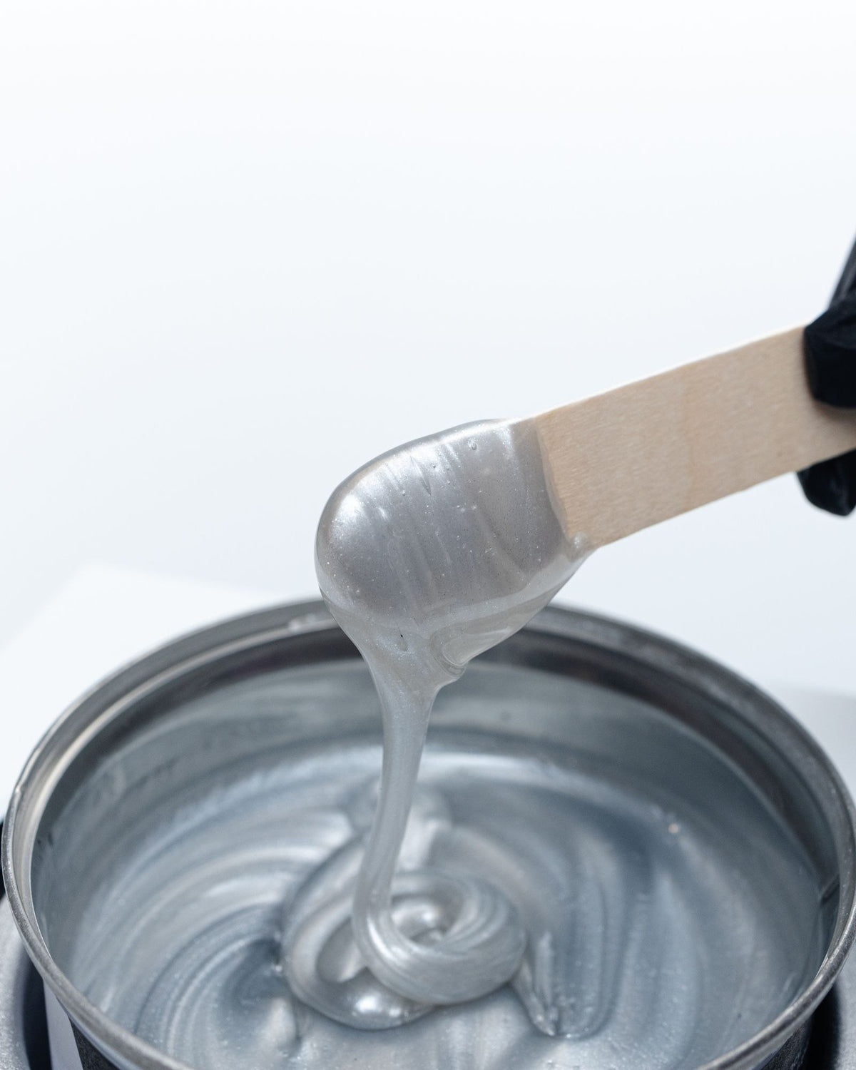 Creamy Nova soft wax running off a spatula back into the warmer, showing the consistency behind a thin, even coat